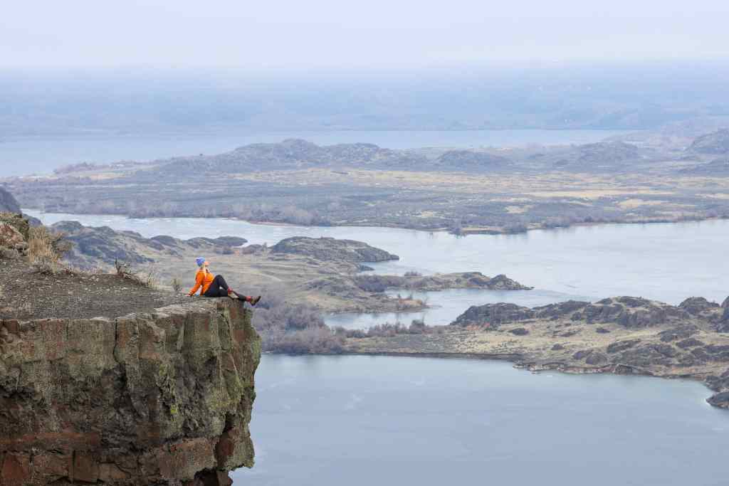 Women in an orange jacket sitting on a cliff side